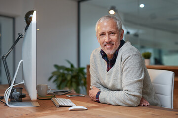 I give mall everyday. Portrait of a smiling mature businessman working on a computer in an office.