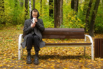 Fototapeta premium person sitting on a bench in the autumn park and drinking tea