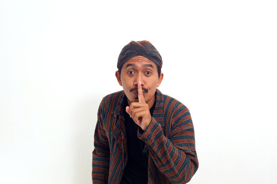 Asian man in java traditional costume brings his hand to his nose as a sign of "silence" gesture
