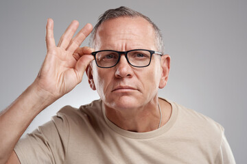 Nothing gets passed me and my extra pair of eyes. Shot of a handsome mature man standing alone against a grey background in the studio and adjusting his glasses.