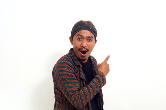 Asian man in javanese traditional costume while pointing something at empty space