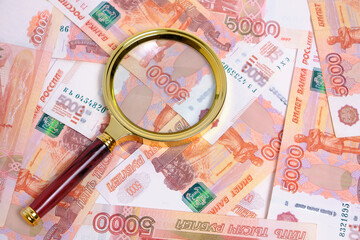 Magnifying magnifier against background Russian rubles with face value five thousand.