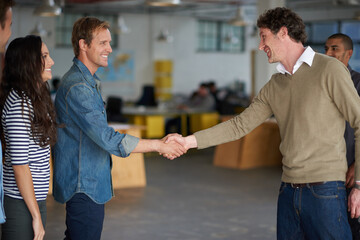 Welcome aboard. Businessmen greeting each other with a handshake in an open office space.