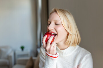 Young beautiful woman eating fresh apple and looking through window.