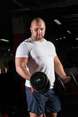 Fototapeta na wymiar Male bodybuilder engaged with dumbbells in the gym