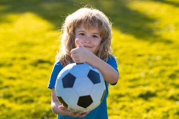 Kid playing soccer, happy child enjoying sports football game, kids activities, little soccer player. Active sporty kid soccer show thumbs up success sign. © Volodymyr