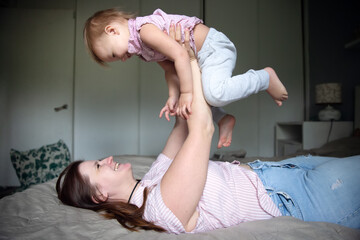 Happy mother with baby toddler on the bed in the bedroom, cozy motherhood and emotions. Bright interior and lifestyle