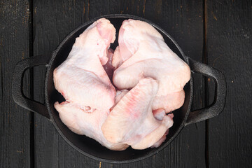 Uncooked chicken wings, in frying cast iron pan, on black wooden table background, top view flat lay