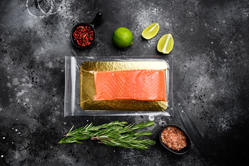 Vacuum packed salmon portion fillet, with herbs, on black dark stone table background, top view...