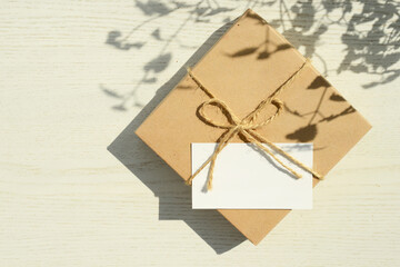 gift box and blank greeting card on a white wooden desk with shadows of grass or plants, copy space