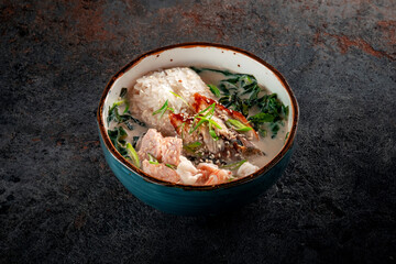 Oriental seafood soup with cream in a blue ceramic bowl. Fish Soup with salmon, eel, shrimp, rice, onion, sesame and seaweed