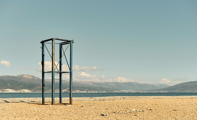 Abandoned lifeguard tower on a pebbly beach, Black Sea coast, empty beach on a sunny day in April. The sky is burnt out at noon, the sea bay in the background is the Caucasian mountains