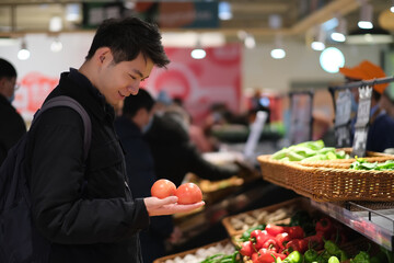 Chinese young man checking vegetable in grocery store. Smiling Asian people shopping in supermarket