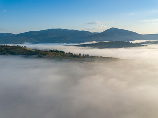 Flight over fog in Ukrainian Carpathians in summer. Mountains on the horizon. A thick layer of fog covers the mountains with a continuous carpet. Aerial drone view.