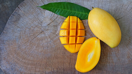 Mango fruit with mango cubes, cut in half and  green leaf on wooden table background.