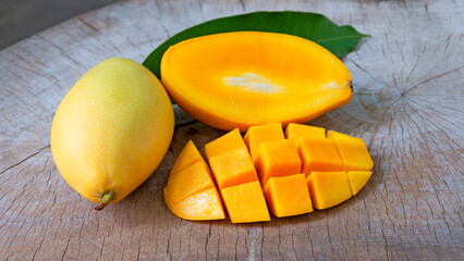 Mango fruit with mango cubes, cut in half and  green leaf on wooden table background.
