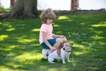Funny child playing with dog in the park. Kid caress dog.