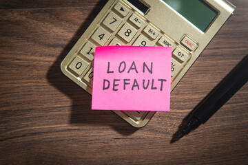 Loan Default on sticky note with a marker and calculator.