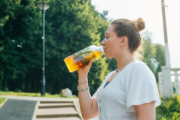 Young woman drinking refreshing herbal drink with lemon after outdoor sport training. Side view of...