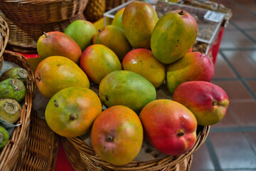Variety of ripe, local, fresh mangoes, identified, on a wicker basket, for sale at a tropical farmers market in Funchal, Madeira, Portugal