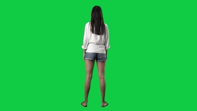 Back view of amazed young woman looking around at copy space. Full body isolated on green screen background