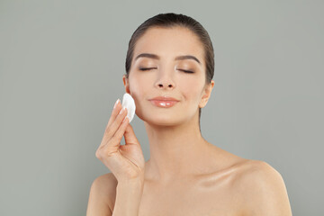 Young attractive woman cleaning her face with a cotton pad and smiling over white background