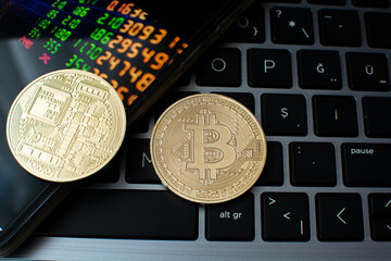 bitcoin coins on laptop keyboard and phone screen.