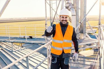 A happy industry worker showing thumbs up for well done job while standing on the height.