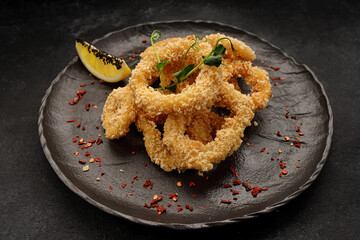 Fried onion rings in batter, on a black plate, on a black background