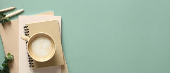 Banner with cup of coffee, stack of paper notebooks and eucalyptus leaves on green background. Home...
