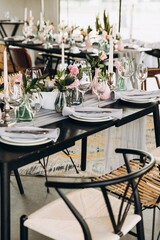 Wedding. Banquet. Decor. Festive tables are decorated with fabric, compositions of flowers and greenery in glass vases, there are candles, glasses, plates and cutlery on the tables