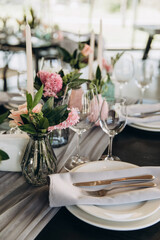 Wedding. Banquet. Decor. Festive tables are decorated with fabric, compositions of flowers and greenery in glass vases, there are candles, glasses, plates and cutlery on the tables