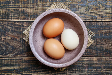 Bowl of fresh farm eggs on wooden background, top view.