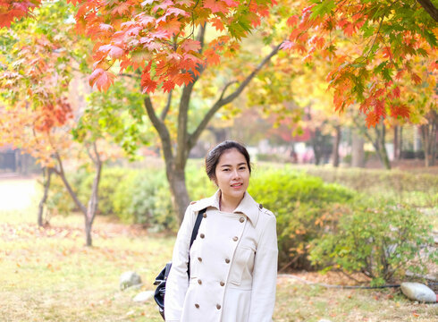 Beautiful tourist girl take photo on colorful autumn tree background in Korea isalnd called Nami island.