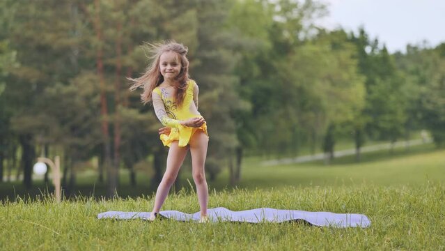 A little girl performs the elements of rhythmic gymnastics in the park.