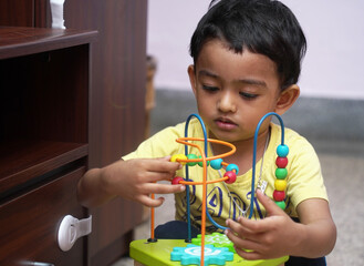 an indian baby boy engaged with a bead puzzle toy, developmental activity milestone concept image