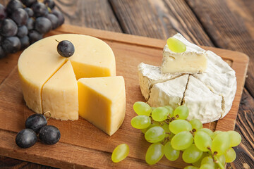 Assorted cheeses,Camembert and gouda cheese on a wooden cutting board with different types of grapes,copy space.