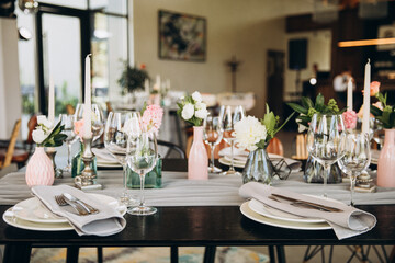 Wedding. Banquet. Decor. Festive tables are decorated with fabric, compositions of flowers and greenery in glass vases, there are candles, glasses, plates and cutlery on the tables