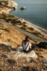 young woman sitting on the ground on the background of the sea coast, sea shore, mountain landscape