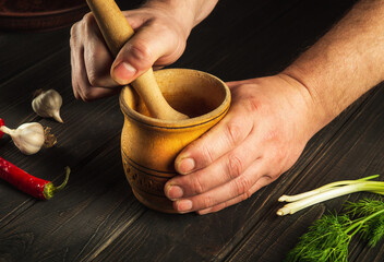 The cook crushing a blending garlic in a wooden pestle and mortar in a close up view on his hands....