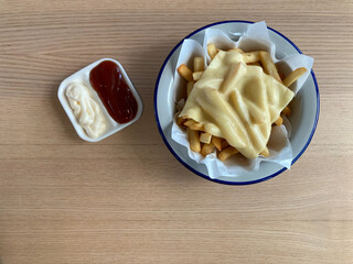 french fries with melted cheddar cheese, served with mayonnaise and ketchup, put on natural brown wood table