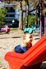 Fototapeta na wymiar Cute baby boy having fun at outdoors playground. Toddler on red plastic slide
