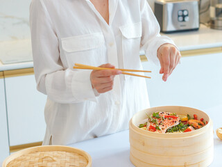 a girl in white clothes cooks steamed food in a bamboo steamer. morning mood, the concept of healthy eating