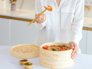 a girl in white clothes cooks steamed food in a bamboo steamer. morning mood, the concept of healthy eating