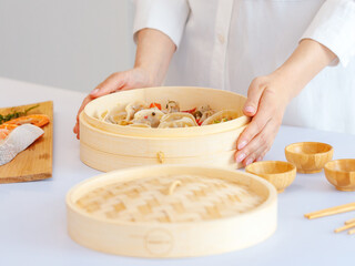 a girl in white clothes cooks steamed food in a bamboo steamer. morning mood, the concept of healthy eating