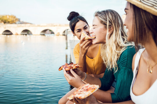 Diverse young women friends eating italian take away pizza in city street - Multiracial female having fun together on summer vacation - Copy space for text - Powered by Adobe