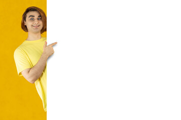 Young man pointing whiteboard for mockup design. Prep Student with long hair. 20s guy on a yellow background. Empty copy space for pasting text