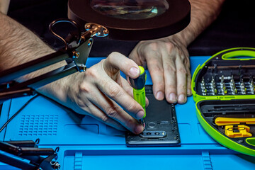 Service and repair of phones and gadgets. Hands of a master with a screwdriver repairing a...