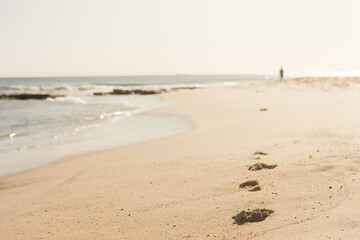 Footprints in the sand on the seashore with a figure blurred in the distance