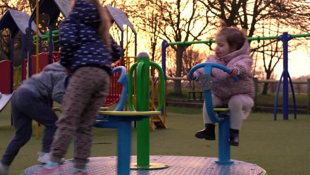 Three little Happy Children having fun spinning on merry-go-round. Smiling Siblings friends playing outside. emotional kids rides on carousel at playground nursery in park.Happy family, childhood